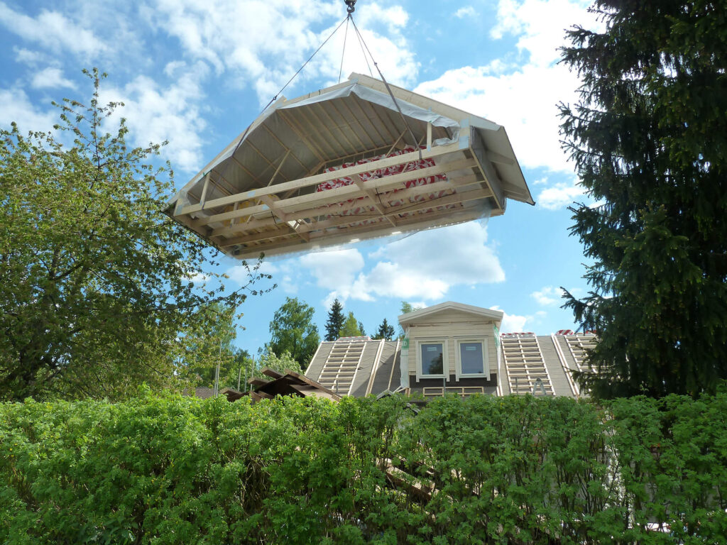 Kran sätter på en färdigbyggd takmodul på ett hus under taklyft.