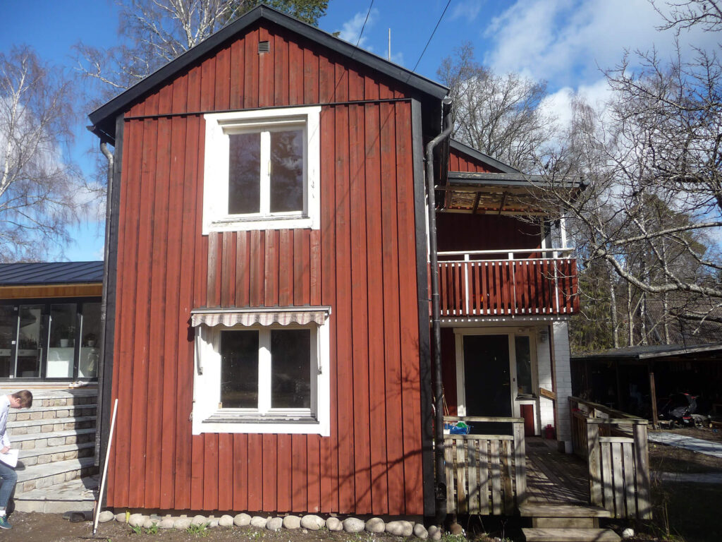 Norrvillan före taklyft – röd trävilla med balkong och gavel med två fönster.