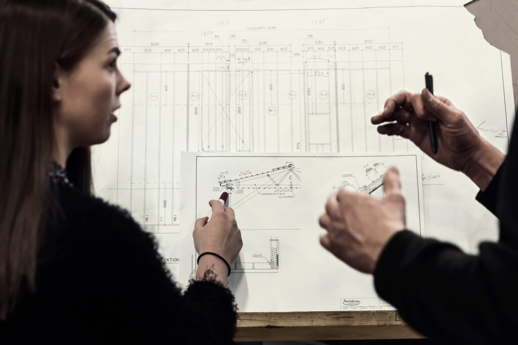Kvinna och man går igenom arkitektritningar för en väggkonstruktion.